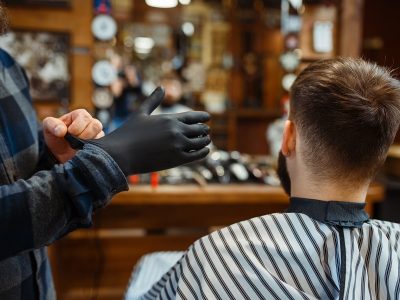 Barber puts on gloves, customer sitting in chair. Professional barbershop is a trendy occupation. Male hairdresser and client in hair salon